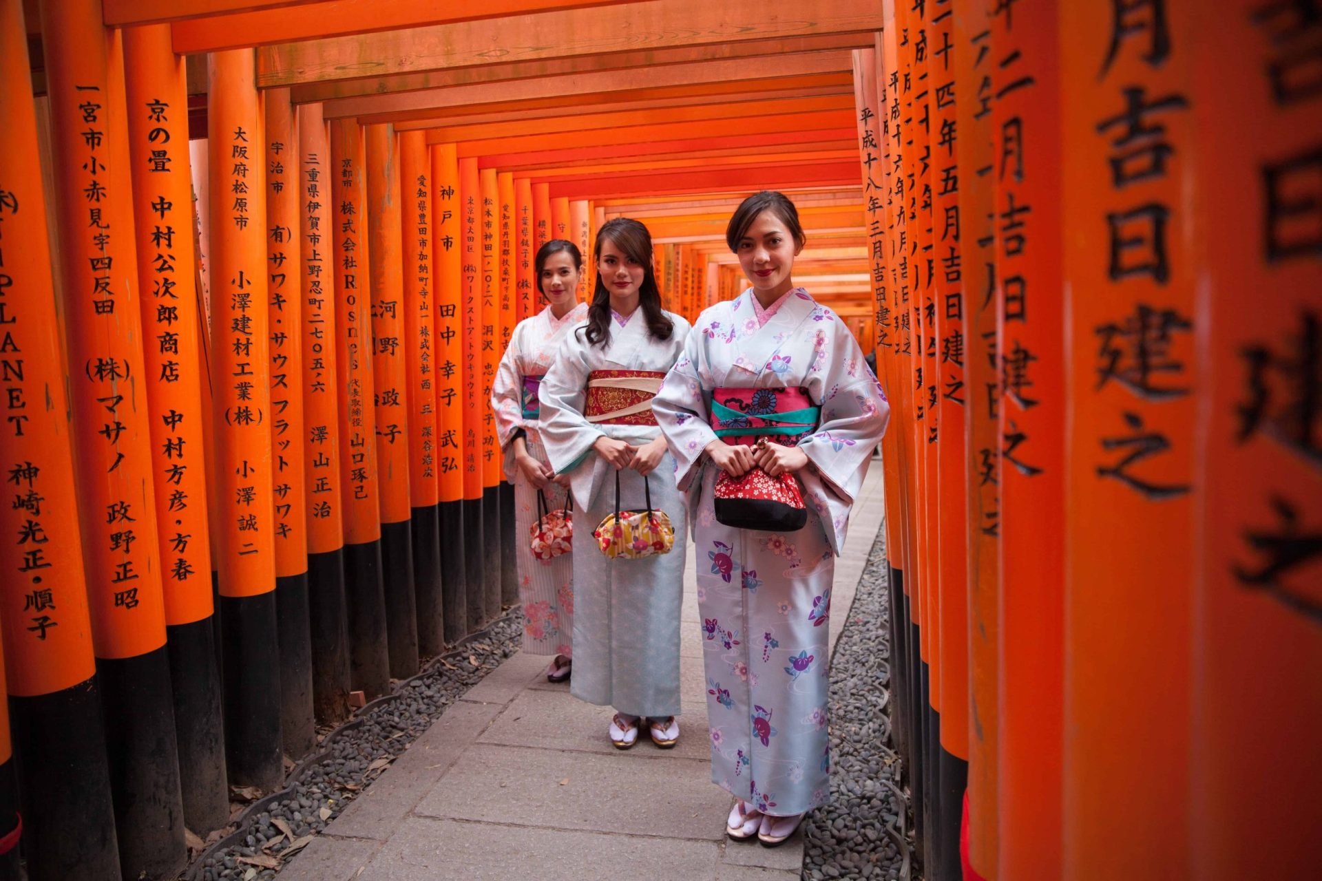 three women in kimono dress surrounded with orange posts